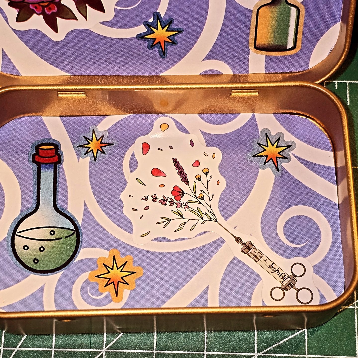 Decorative tin with botanical design, beakers, and stars on a purple background
